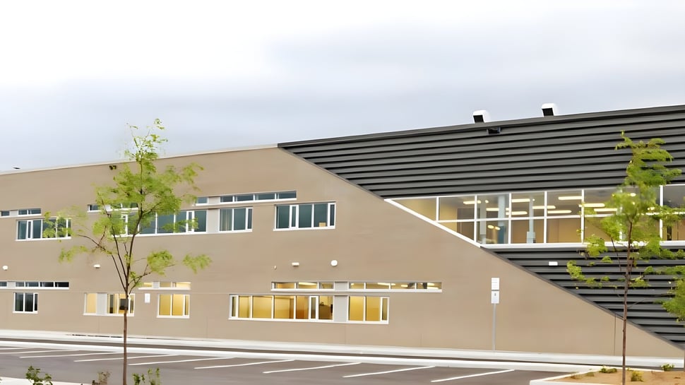 El moderno edificio de varios pisos de la Maple Ridge Secondary School en Ontario está rodeado de árboles y un estacionamiento.