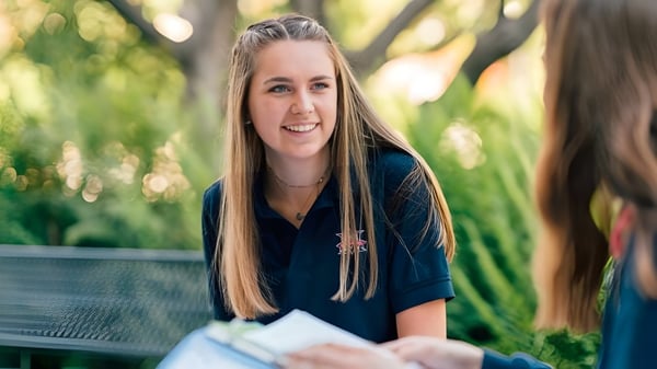 Una estudiante de la Maranatha High School está sonriendo en una zona exterior verde con árboles de fondo.