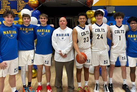Estudiantes de la Marian Catholic High School posan juntos en el gimnasio con un fondo de baloncesto.