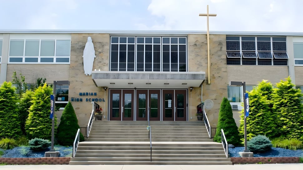 El gran edificio de ladrillo de la Marian Catholic High School con una cruz en el techo está rodeado de áreas verdes.