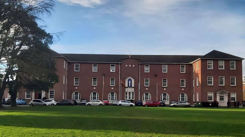 El edificio de ladrillo de varios pisos con arcos en el campus del Marian College bajo un cielo nublado.