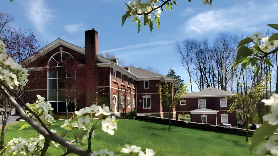 El edificio de ladrillo con torre de la Marianapolis Preparatory School está incrustado en un paisaje verde con árboles en flor.