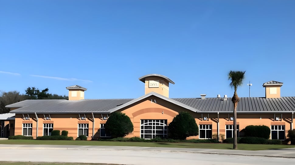 El edificio de ladrillo con techo de metal y chimeneas de Marion County Public Schools está rodeado de árboles y áreas verdes.