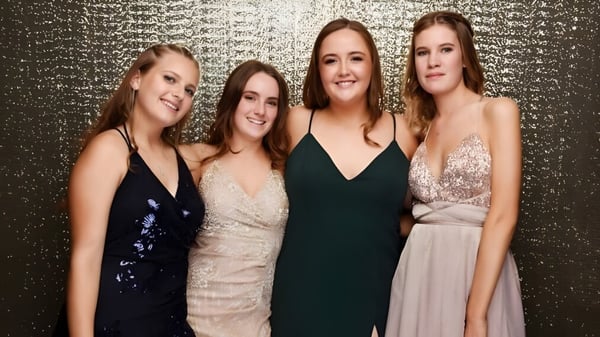 Cuatro estudiantes en ropa formal posan frente a un fondo dorado en el campus del Marist College.