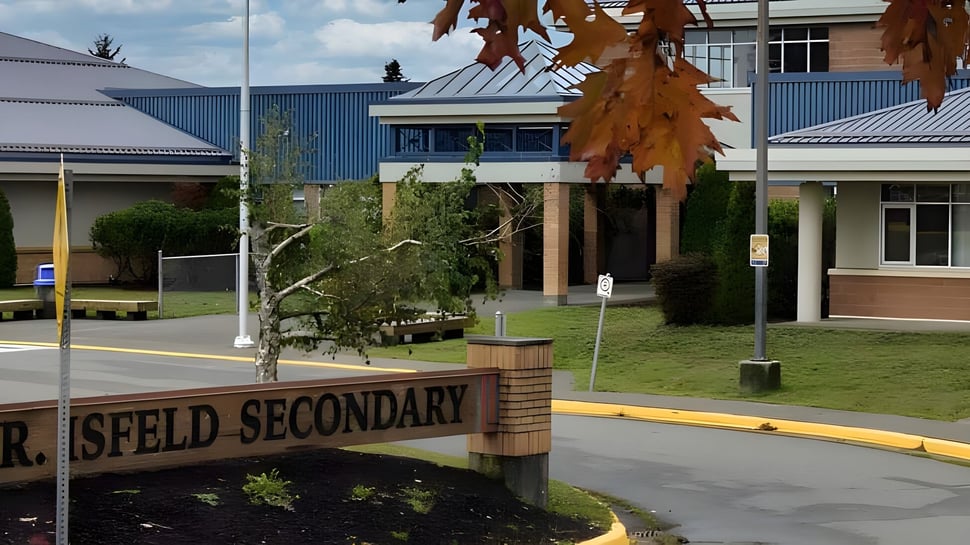 El campus de la Mark R. Isfeld Secondary School con un cartel de camino escolar y rodeado de árboles y edificios coloridos.