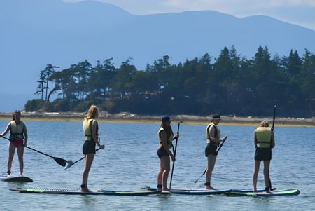 Estudiantes de la Mark R. Isfeld Secondary School haciendo paddleboarding en un lago rodeado de bosques y montañas.