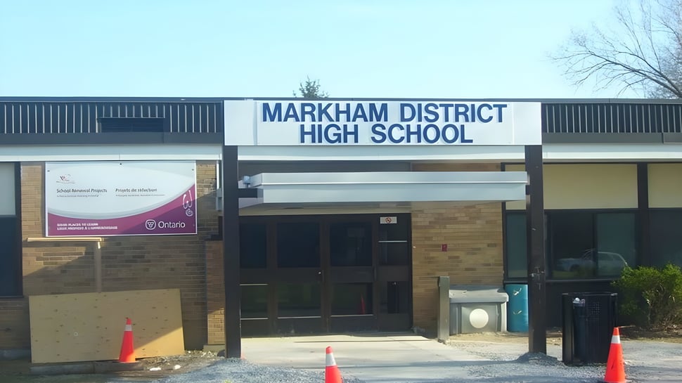 El edificio de ladrillo de la Markham District High School con un letrero llamativo se encuentra frente a árboles y un cielo despejado.