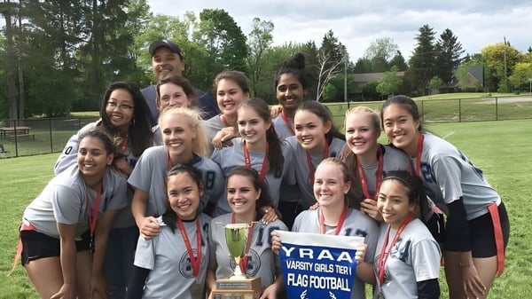 Un grupo de jóvenes deportistas de la Markham District High School celebra en una cancha con un trofeo.