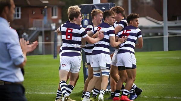 Un grupo de jóvenes atletas en camisetas a rayas está en el campo de deportes del Marlborough College frente a un edificio.