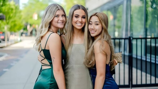 Tres estudiantes de Marlborough Girls están juntas al aire libre y sonríen frente a una barandilla con vegetación de fondo.