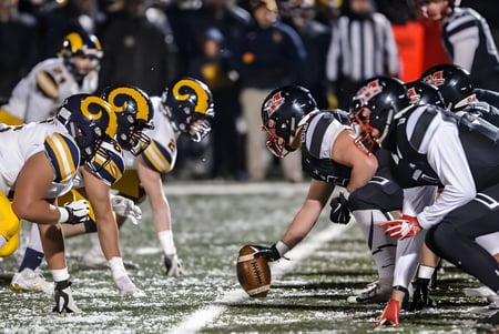 Estudiantes de la Marquette High School están listos en uniforme de equipo para la próxima jugada en el partido de fútbol americano.