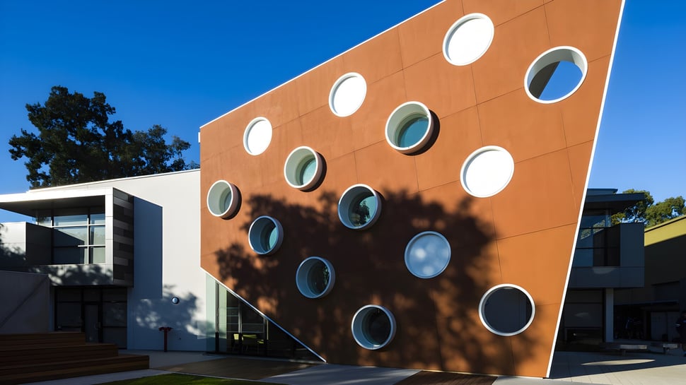El edificio naranja de la Marryatville High School con ventanas redondas y sombras de árboles en la fachada se ve contra un cielo azul.