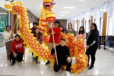 Un grupo de estudiantes con ropa tradicional china con un gran disfraz de danza del dragón en el pasillo de la Martin Luther High School.