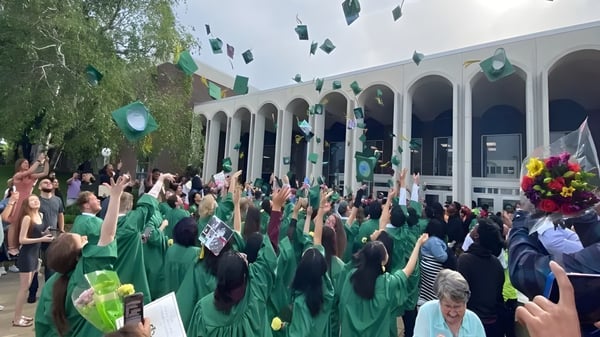 Un grupo de personas vestidas de verde se reúne frente al edificio de la Martin Luther High School con arcos y columnas.