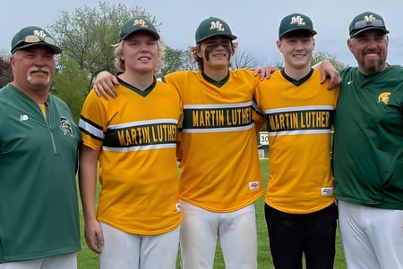 Cinco estudiantes de la Martin Luther High School están juntos al aire libre en uniforme de béisbol bajo un cielo azul.
