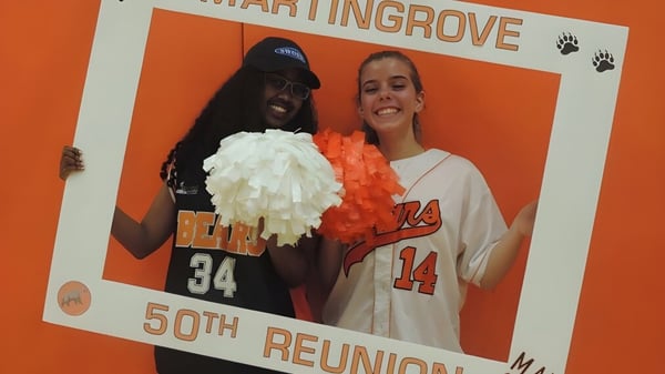 Dos personas posan frente a un fondo naranja con texto por el 50 aniversario en el Martingrove Collegiate Institute.