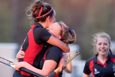 Dos alumnas de The Mary Erskine School en uniformes deportivos se abrazan en el campo de deportes.