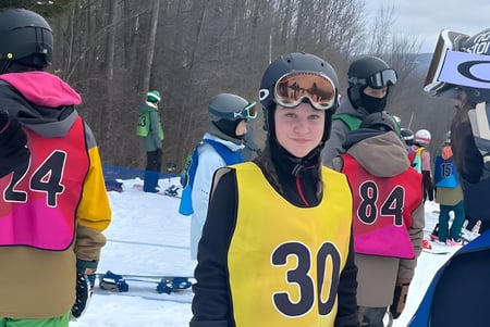Un grupo de estudiantes de la Marymount Academy lleva ropa de esquí colorida y cascos y está de pie en una pendiente nevada con árboles.
