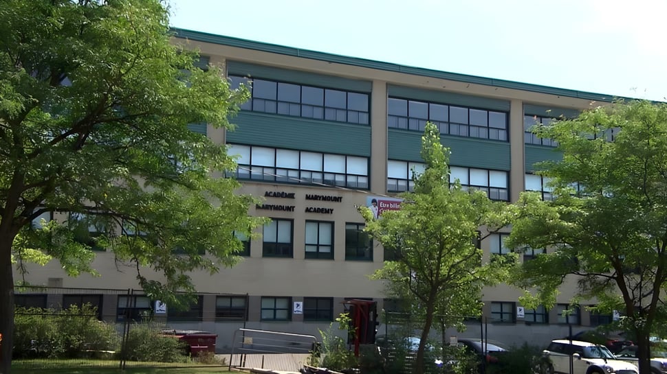 El edificio de varios pisos pintado de verde de la Marymount Academy International está rodeado de árboles verdes.