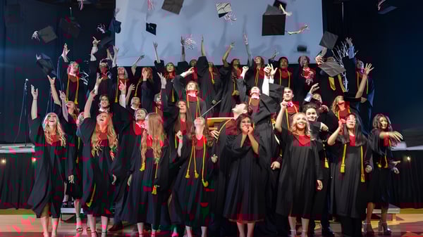 Un grupo de estudiantes de la Master's Academy and College está de pie en togas negras y con cintas rojas en un escenario durante la ceremonia de graduación.