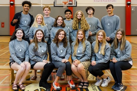 Estudiantes de la Master's Academy and College están sentados juntos en el gimnasio y posan para una foto de equipo con uniformes escolares grises.