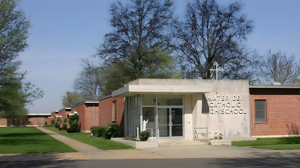 El moderno edificio de ladrillo de la Mater Dei Catholic High School se encuentra en un área verde con árboles bajo un cielo despejado.