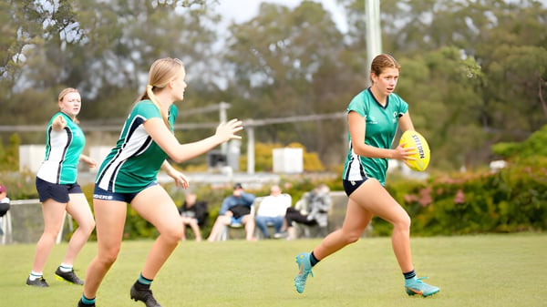 Estudiantes del Matthew Flinders Anglican College juegan en el campo deportivo rodeados de árboles y vegetación.
