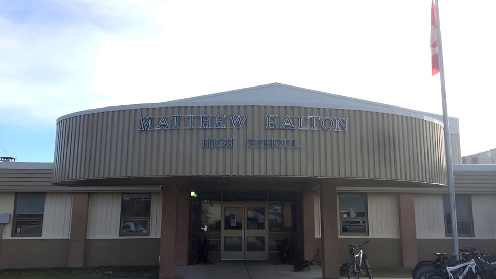 El edificio en forma de cúpula gris de la Matthew Halton High School con el letrero en la entrada principal y una bicicleta delante.