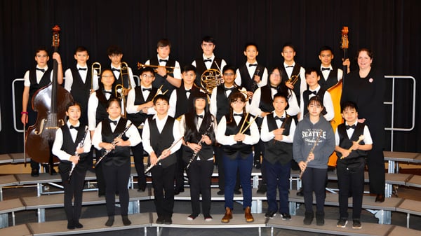 Un grupo de estudiantes de la Matthew McNair Secondary School está de pie en ropa formal en un escenario frente a un fondo oscuro.
