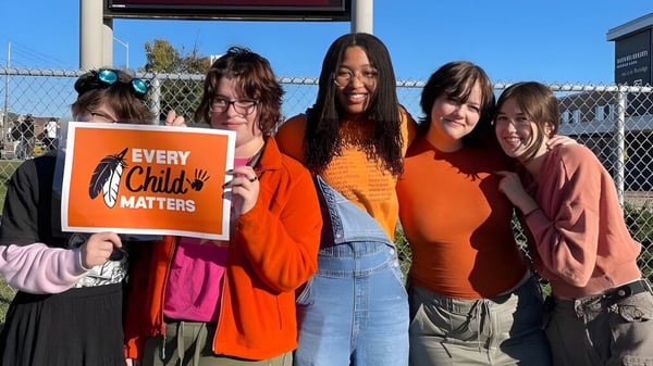 Un grupo de jóvenes con un cartel 'Every Child Matters' está frente a una cerca en el terreno de la Maxwell Heights Secondary School.