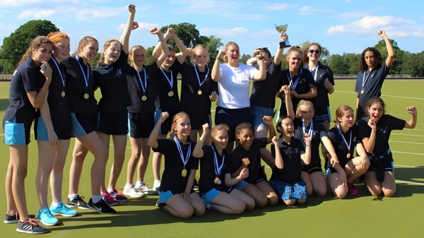 El equipo femenino de la Mayfield School celebra su éxito juntos en el campo deportivo con los brazos en alto.