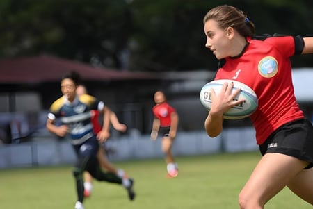 Una jugadora de rugby de la Mayfield School corre con el balón en el campo de césped durante un partido.