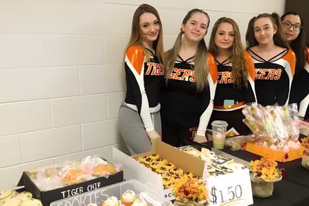 Un grupo de alumnas de la McNally High School está juntas frente a una pared y venden diferentes objetos.