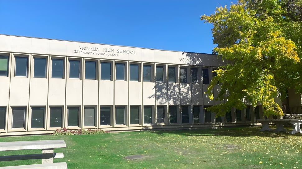 El moderno edificio de varios pisos de la McNally High School está rodeado de vegetación verde bajo un cielo azul.