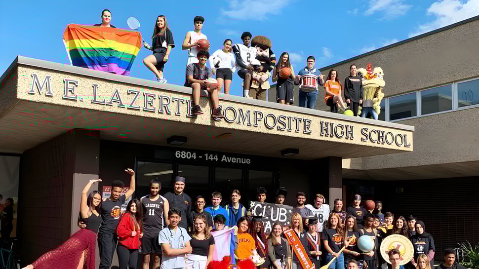 Estudiantes y personal de la M.E. LaZerte Composite High School están frente al edificio escolar con una clara bandera del arcoíris.