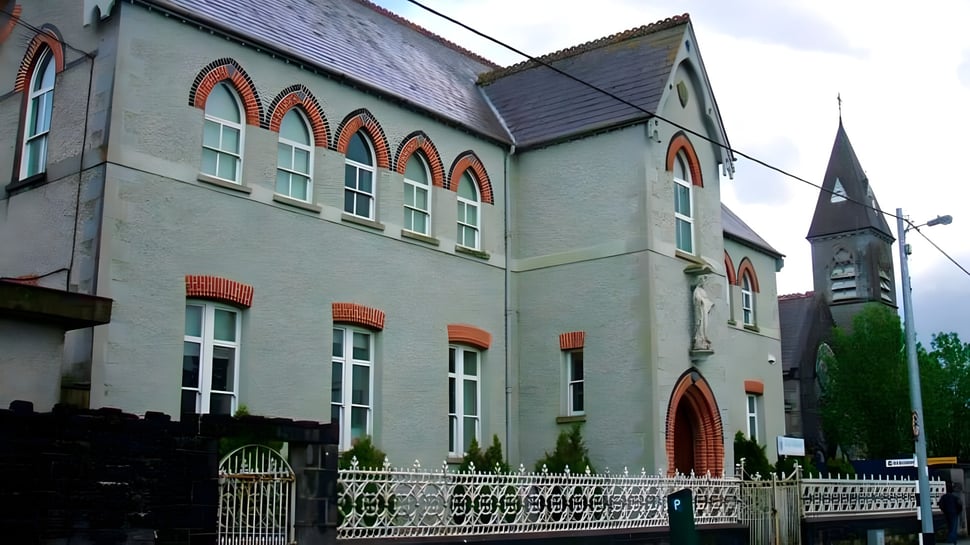 El edificio de la Meán Scoil Mhuire Longford muestra una fachada de ladrillo decorada con altas ventanas y una torre.
