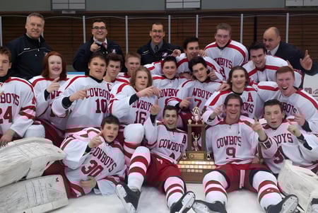 El equipo de hockey de la Medway High School posa con un trofeo en un gimnasio.