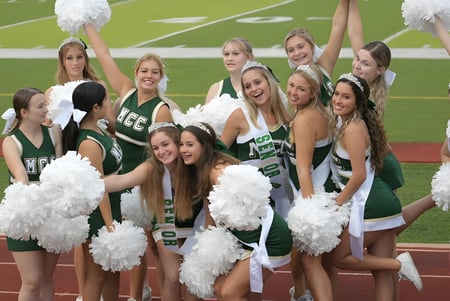 Un grupo de cheerleaders de la Melbourne Central Catholic High School posan juntas en el campo de deportes con pompones en alto.
