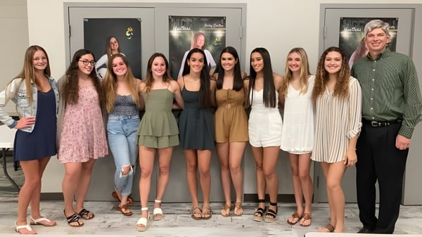 Un grupo de estudiantes se encuentra frente a un edificio en el campus de la Melbourne Central Catholic High School con un hombre al fondo.