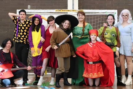 Un grupo de estudiantes de la Melville Senior High School posando con disfraces coloridos y vibrantes frente a una pared de ladrillos.