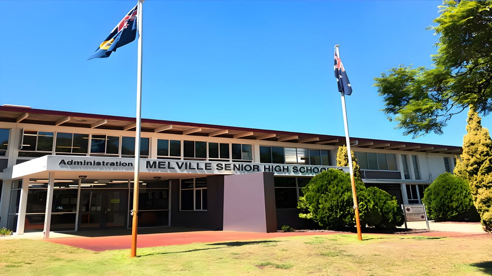 La entrada principal de la Melville Senior High School con la bandera australiana y la bandera de Australia Occidental en primer plano y árboles al fondo.