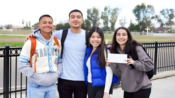 Cuatro estudiantes del Merced Union High School District están afuera en un área parecida a un parque con árboles y barandillas.