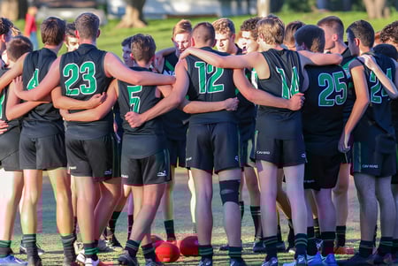 Un grupo de jóvenes atletas del Mercedes College está en un huddle en un campo de césped.