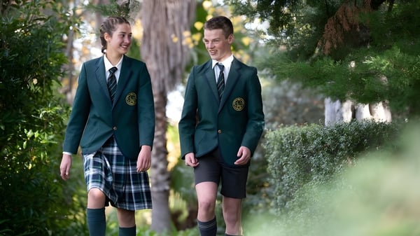 Dos estudiantes en uniformes escolares caminan juntos por un camino rodeado de exuberante vegetación en el campus del Mercedes College.