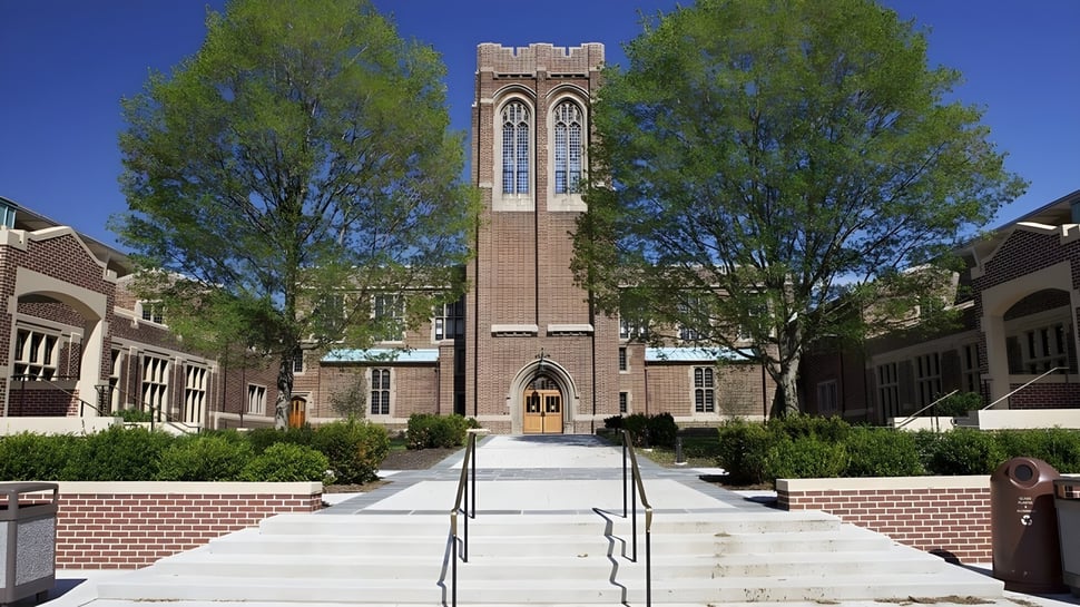 La torre gótica de ladrillo de la Mercersburg Academy está rodeada de vegetación verde y un camino pavimentado.