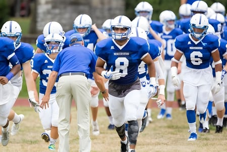 Un grupo de futbolistas en uniformes azules y blancos corre juntos en el campo de la Mercersburg Academy.