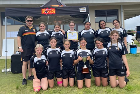 Un grupo de jóvenes atletas está frente a una tienda en el campo deportivo de la Mercury Bay Area School.