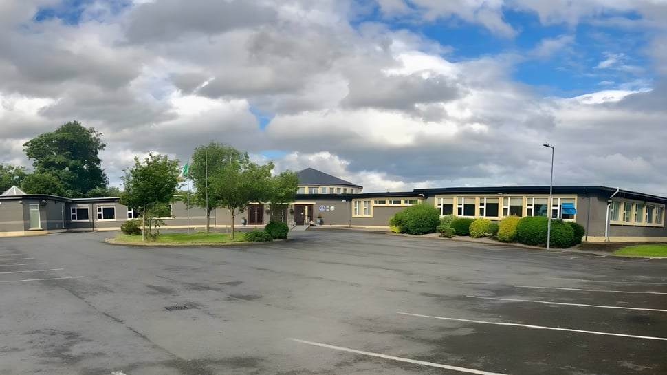 El estacionamiento pavimentado en el terreno del Mercy College está rodeado de árboles y edificios bajo un cielo nublado.