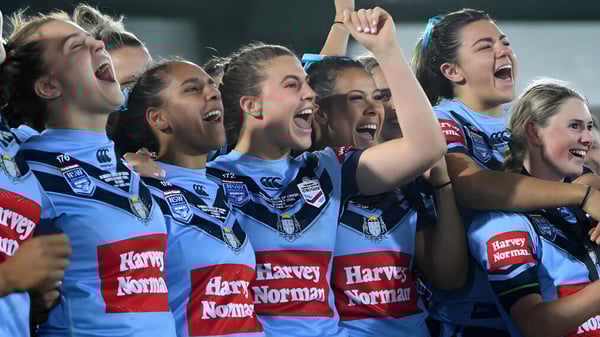Un grupo de atletas femeninas celebra juntas en el campo deportivo del Mercy College con los brazos en alto.