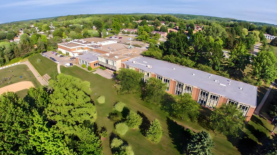 El extenso terreno de la Mercyhurst Prep School se extiende con edificios y paisajes verdes entre colinas bajo un cielo azul.
